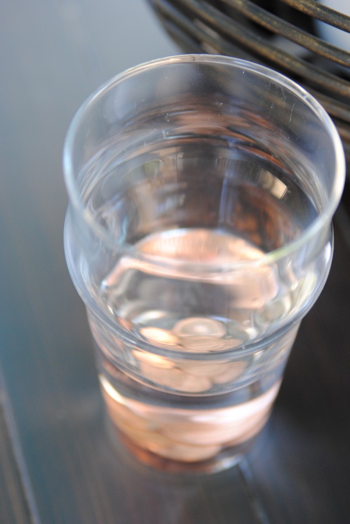 A full glass of water with pennies at the bottom 