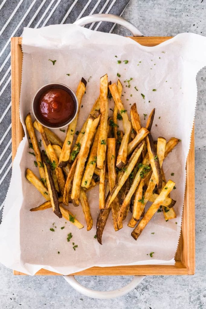 homemade french fries in wax paper in a wood serving dish with a ramekin of ketchup
