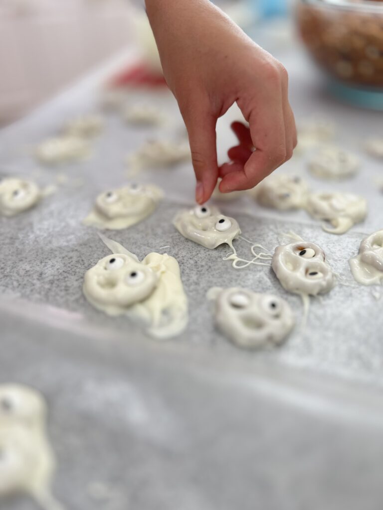 adding candy eyes to chocolate covered pretzel ghosts