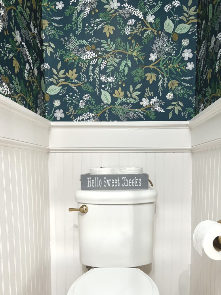 toilet with gold handle and beadboard paneling with Rifle Paper Co peel-and-stick wallpaper Juniper Forest 