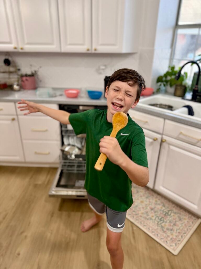 singing in the kitchen with a wooden spoon while unloading the dishwasher
